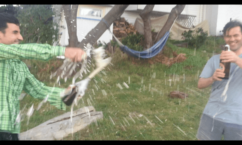 Photo of two people popping very fizzy bottles of beer in celebration.