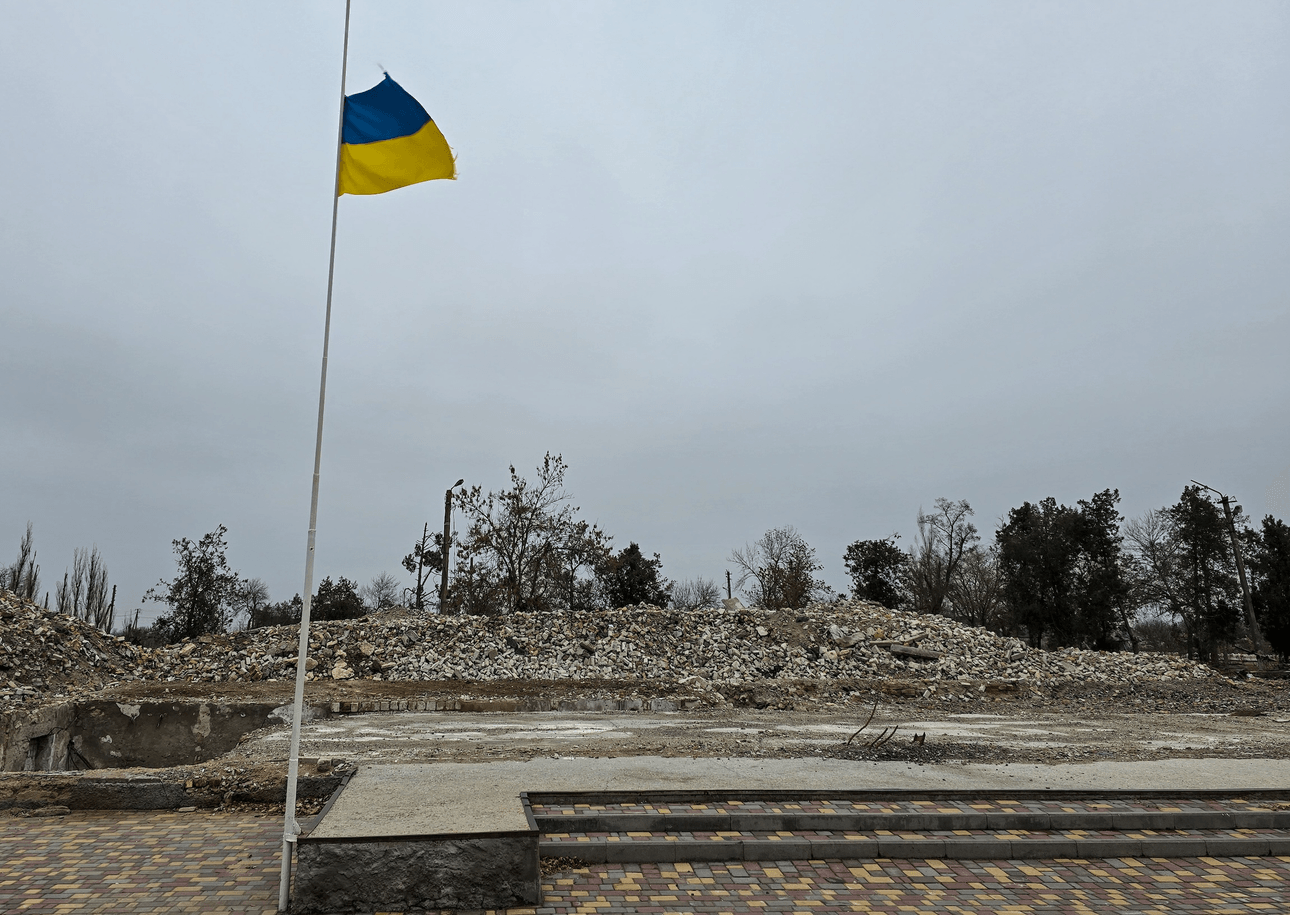 A Ukrainian flag flutters in the breeze in front of a pile of rubble