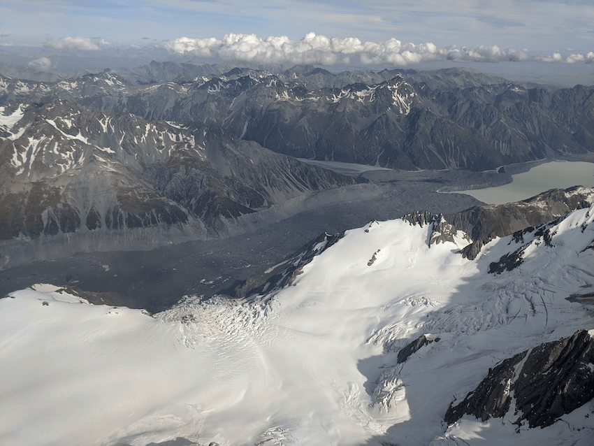 a view from a small plane window of a glacier covered in stones and snowy mountains