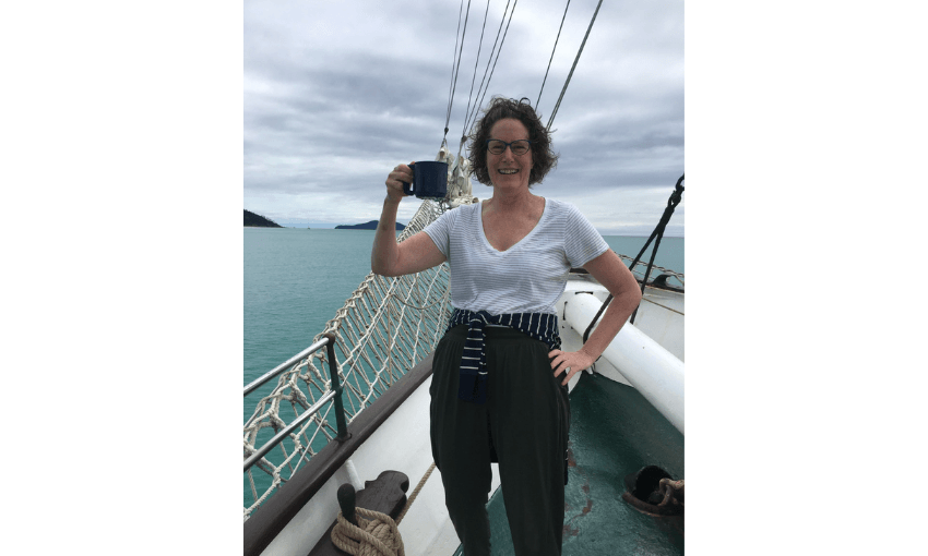 A photograph of Kate Camp on a yacht raising a mug in cheers.