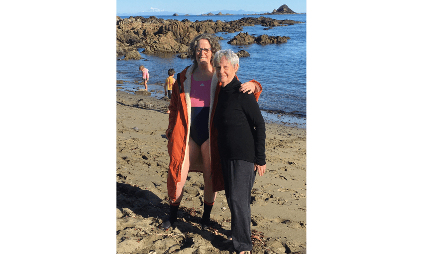 A photo of Kate Camp with her mum on the beach. Kate has one arm around her mum. 