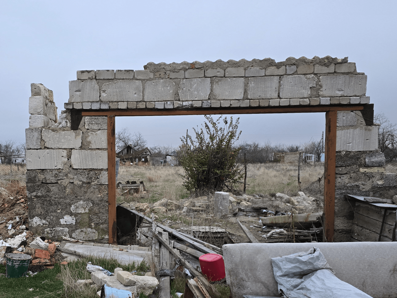 A wall of concrete blocks stands alone, surrounded by rubble