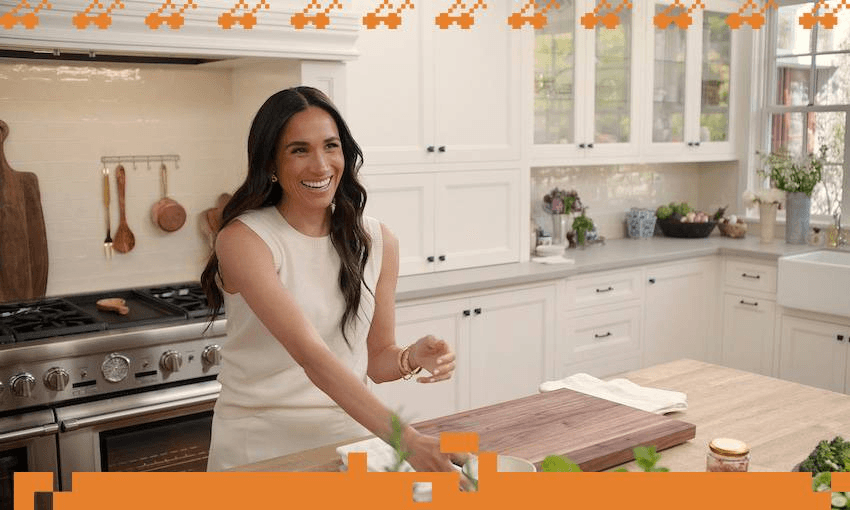 Meghan Markle stands in at the bench in an all white kitchen and prepares to make a meal