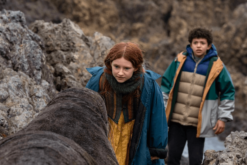 A young girl with red hair and a blue coat and a boy wearing a puffer jacket come face to face with a seal on some rocks at a Wellington beach