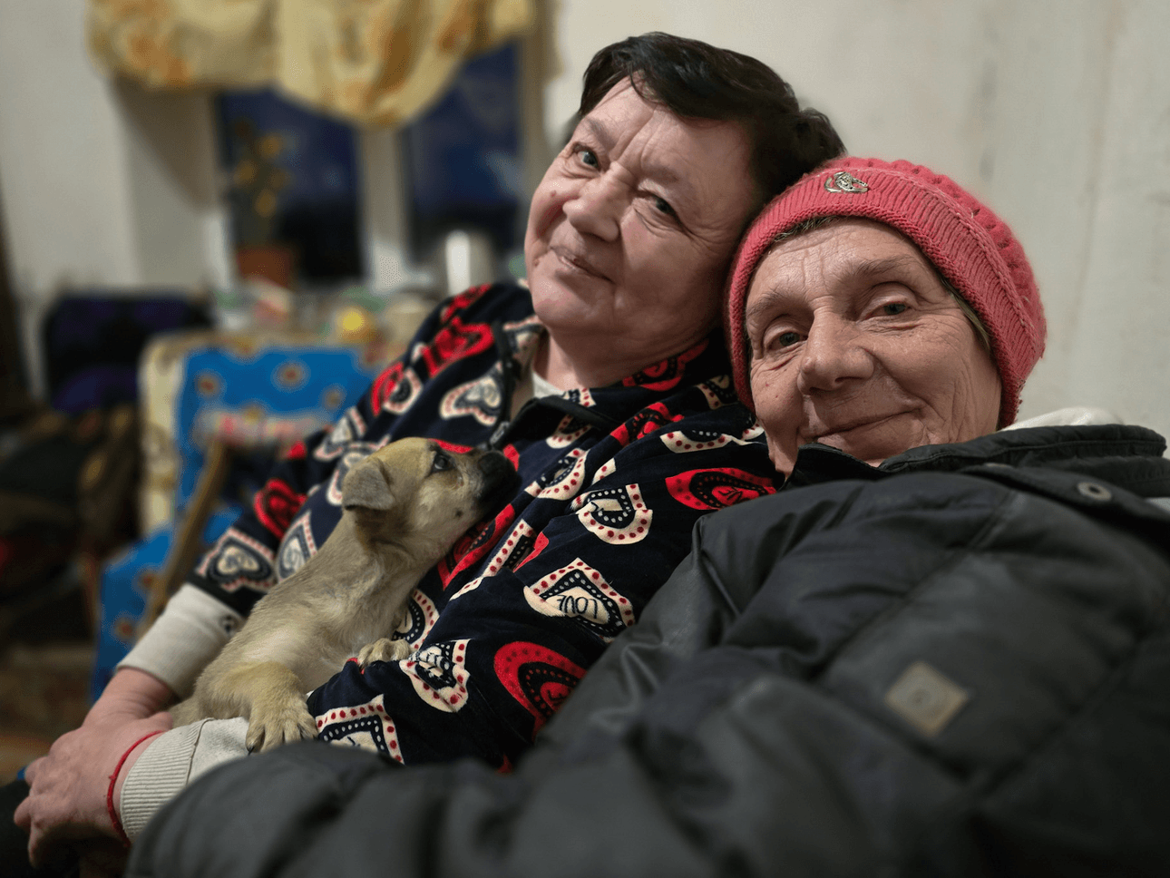 Two women hold a small puppy and wear warm clothing
