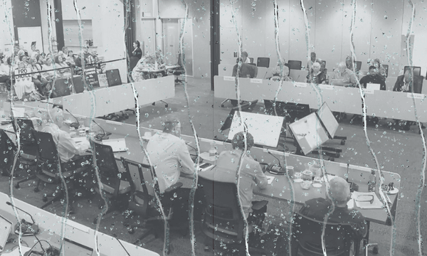 a meeting room filled with people seated at desks in a U shape. Dripping water is overlaid on top.