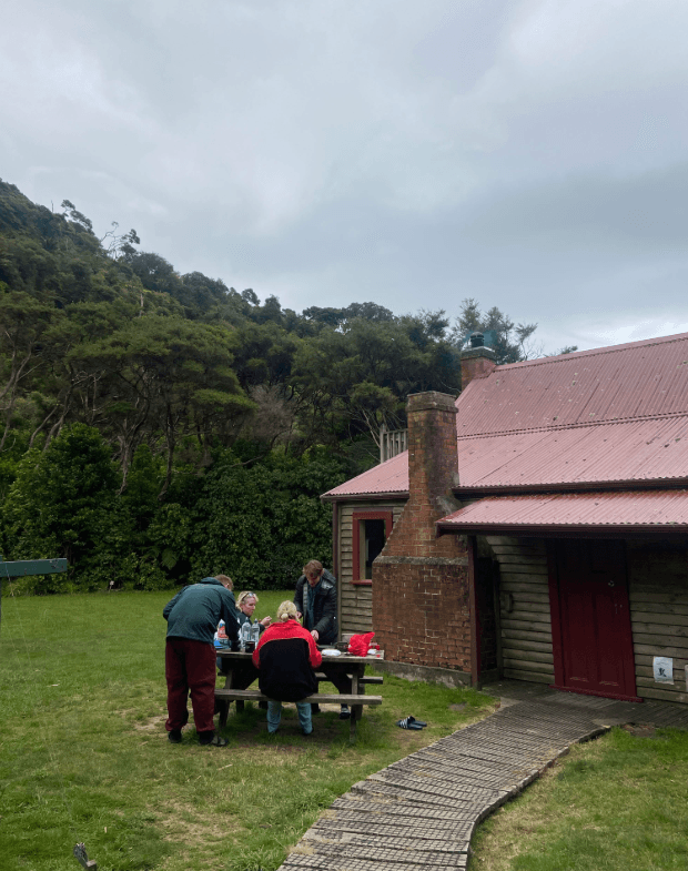 a group of hikers sit at a table outside a DOC hut