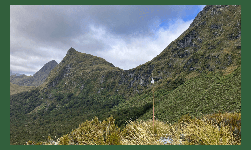 a dark green background with a little orange pole the only signs of human habitation visible with a dark steep and spiny ridge sidling into the sky