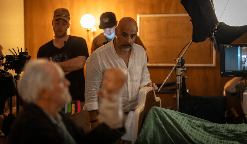 James Ashcroft surrounded by film crew watches John Lithgow hold up a scary doll puppet