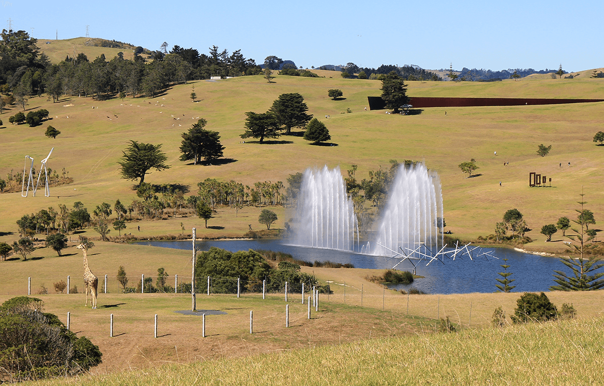 pastoral landscape with big artworks including a jet water fountain, a bit steel wall and a life-like sculpture of a giraffe