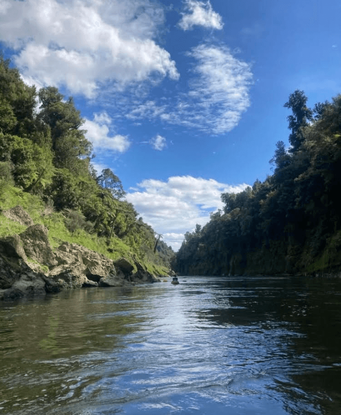 the whanganui river with steep hills on either side and a blue sky above