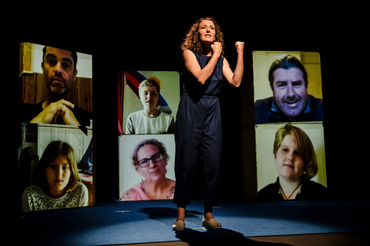 A woman on stage with six boxes behind her, On each box a face of a family member is being projected.