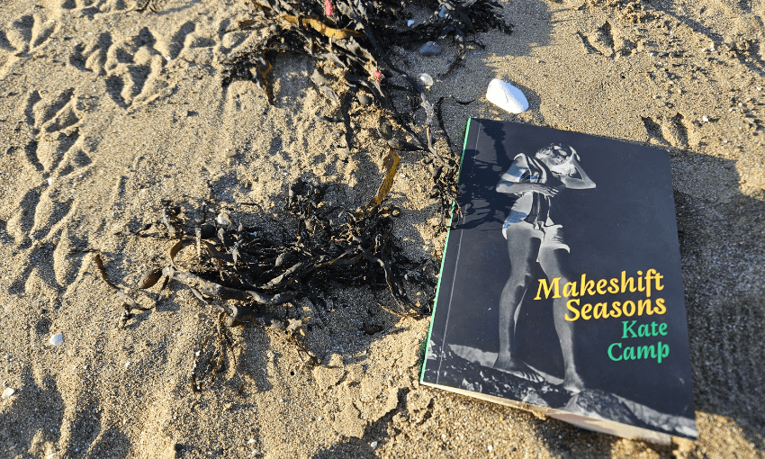 A photo of the cover of Kate Camp's poetry book, Makeshift Seasons, on a beach.