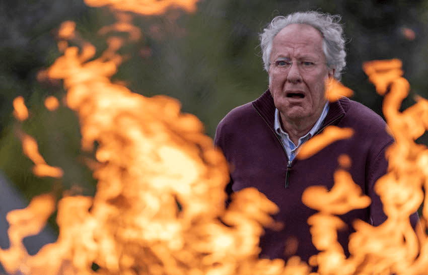 Geoffrey Rush peers through flames with a terrified expression