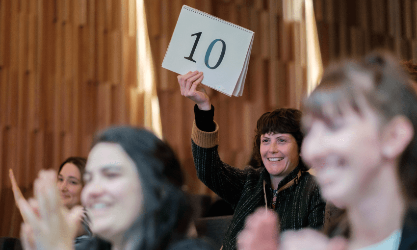 A photo of a crowd. One woman is holding up a sign that says the number 10. She is smiling.