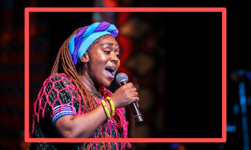 a black woman with a colourful headband sings into a microphone, spotlit on stage