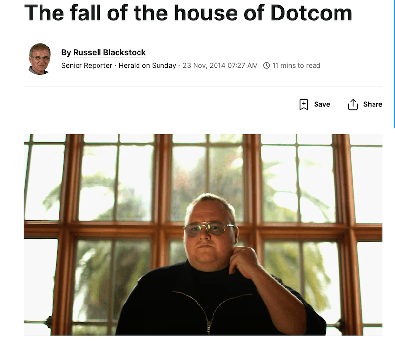 Man in dark clothing, wearing glasses, stands in front of large windows with palm trees visible outside.