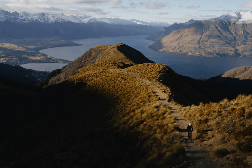 golden light illuminating the tussocky upland of the benlomond ridge, with Benhildred a small dot making his way uphill, Lake Wakatipu dark and blue far below