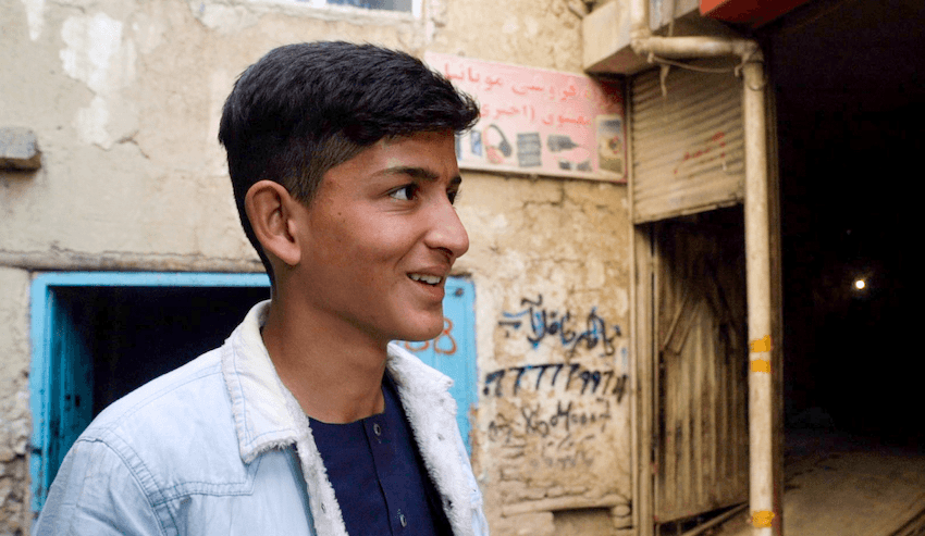 A young man smiles off camera against a worn and grafitti'd wall