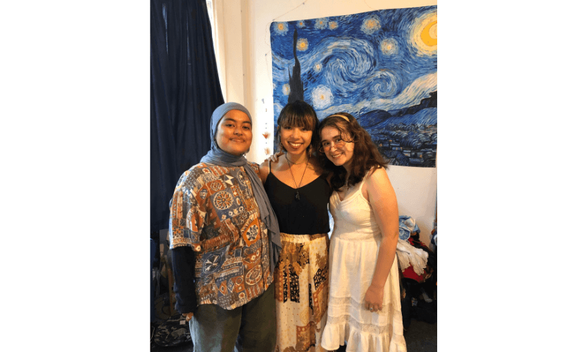A photograph of three friends standing in a bedroom with a picture of Starry Night by van Gogh in the background.