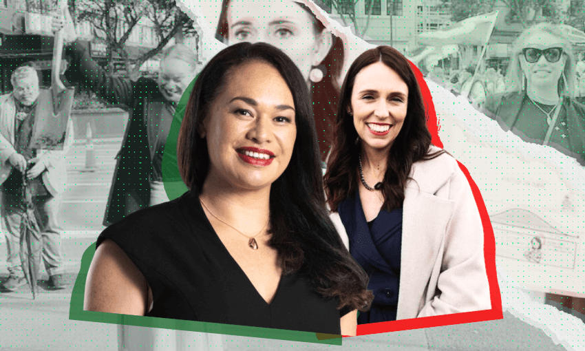 Two women stand in the foreground, smiling. The woman on the left has long dark hair and wears a black top; the woman on the right has long brown hair and wears a navy blazer. A faded crowd is in the background.