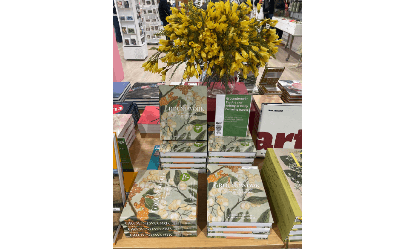 A photograph of books displayed on a table with a big bunch of flowers behind them. 