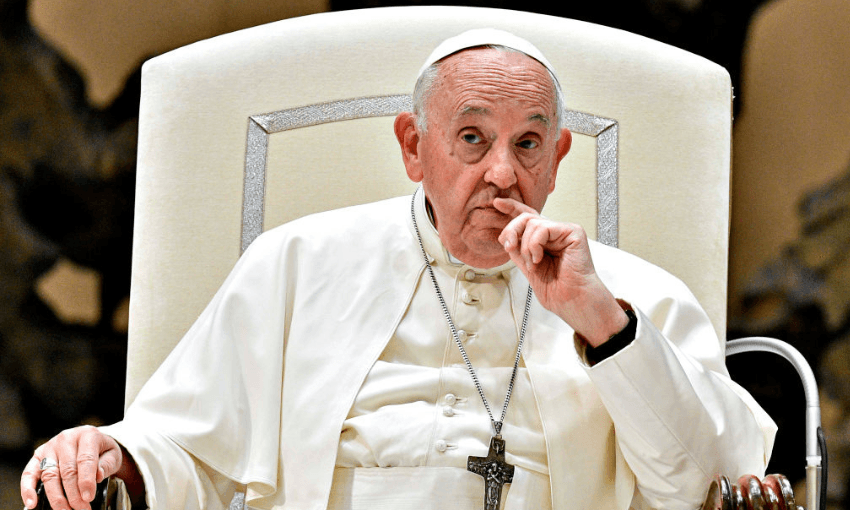 An elderly man (Pope Francis) wearing white papal robes and a skullcap sits on a large chair, resting his hand near his mouth, looking thoughtful. A large cross necklace hangs from his neck.