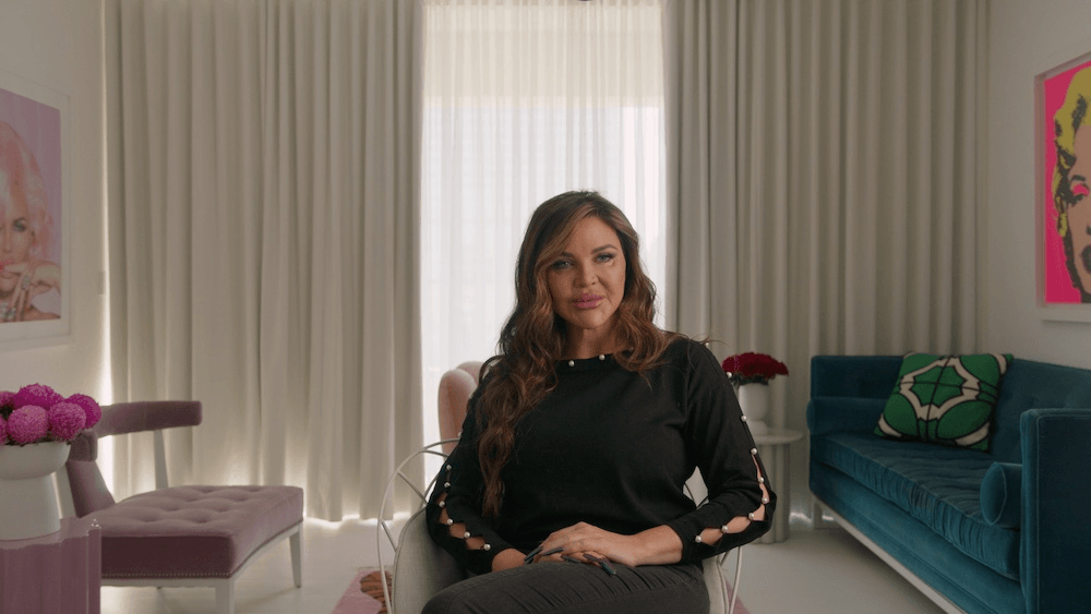 a woman in a black dress being interviewed in an apartment