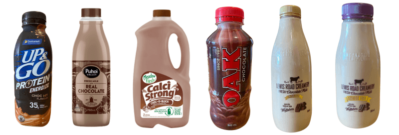 Six bottles of chocolate milk are lined up. From left to right: Up&Go Protein, Puhoi Valley Real Chocolate, Calci Strong, Oak Plus Chocolate, and two glass bottles with indistinct labels, one being lighter in color.