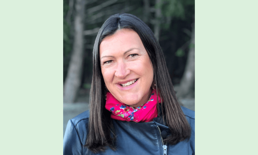 a white whoman with dark hair wearing a pink scarf with trees in the background smiling slightly