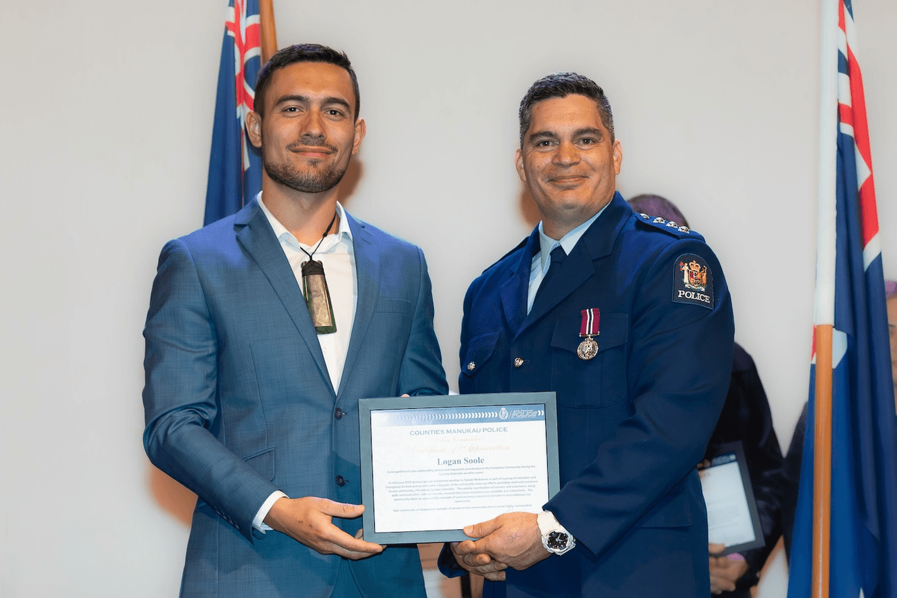 Two men hold a certificate, one a police officer in uniform and the other in a blue suit