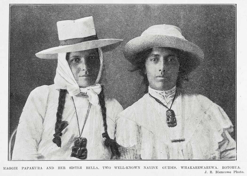 Two Māori women in white dresses and wide-brimmed hats, both wearing pounamu pendants. The photograph is black and white and captioned as Maggie Papakura and her sister Bella, guides from Rotorua.