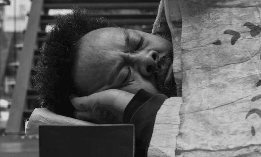 Kalisolaite ‘Uhila sleeps lies on his side, eyes closed, resting his head on his hand and covered with a blanket. The image is in black and white.