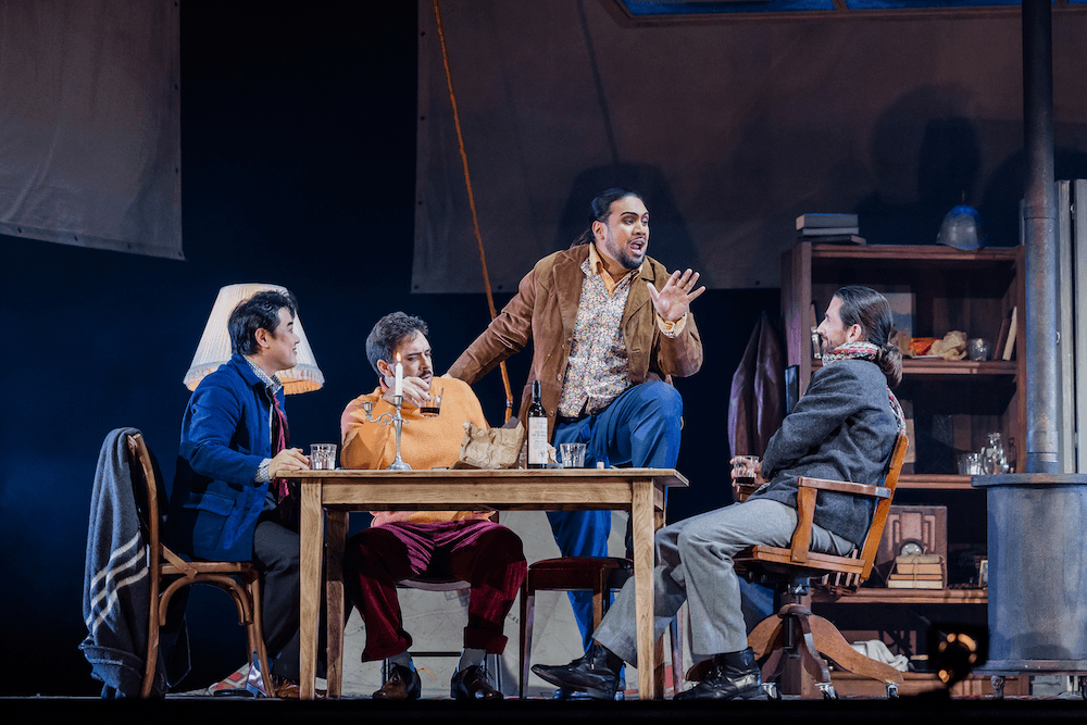 the cast of la boheme sit around a table on stage