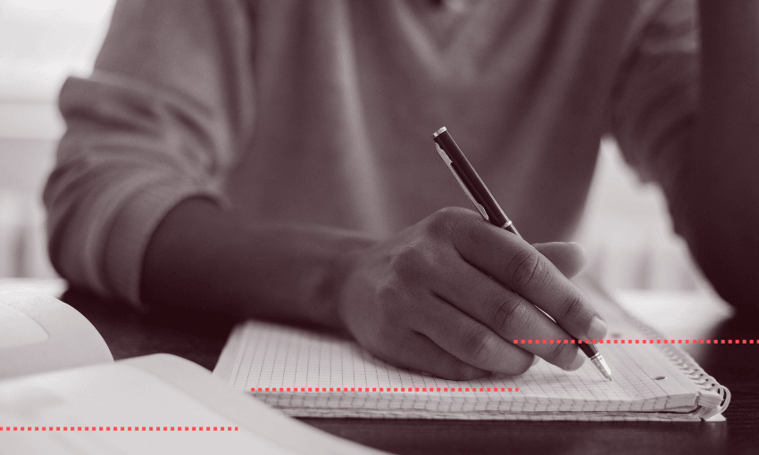 A greyscale photograph of a student writing with a pen, on lined paper.