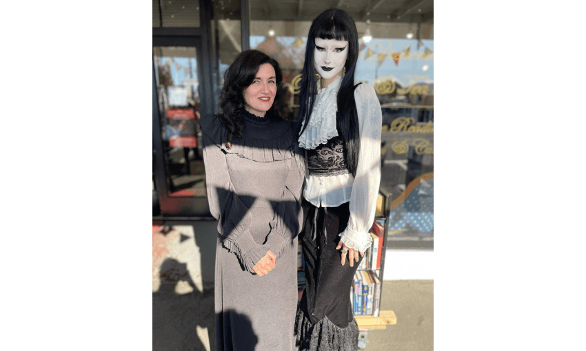 A photograph of Noelle McCarthy standing outside a book shop wearing a black gothic style dress; standing next to a tall young woman in full gothic make up and clothes.