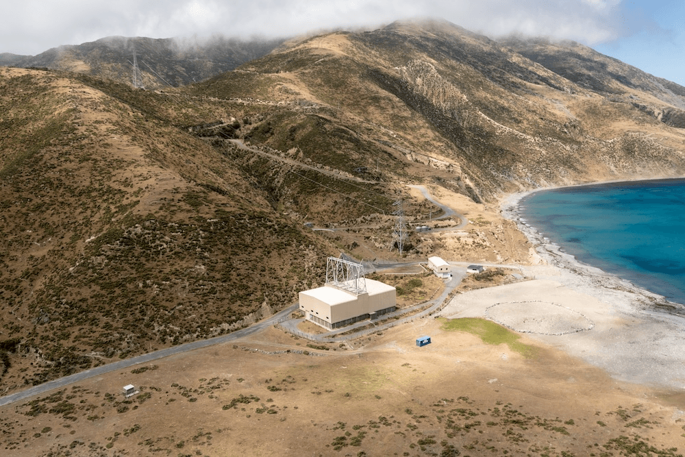 brown scrubby hills and a little white substation next to a turquoise curve of water