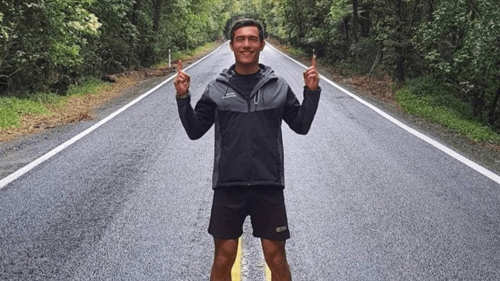 A man stands in the middle of a road with his hands up, smiling