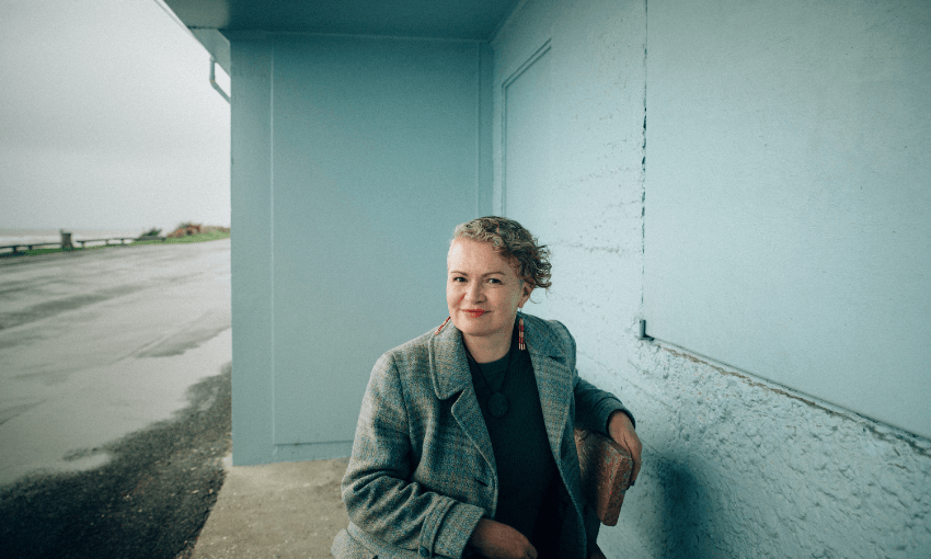 A photograph of a woman, smiling in an outdoor setting with pale green background.