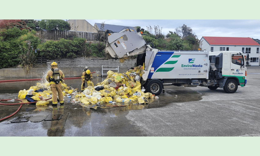a green background and a rubbish truck with contents on the road surrounded by firefighters