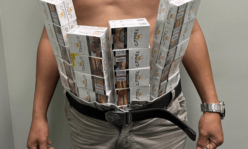 A person wearing dozens of stacked Camel cigarette packs strapped to their bare chest and waist with a belt, standing against a plain background.