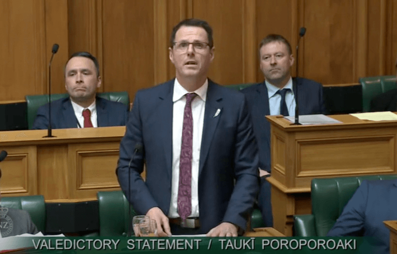 A man in a suit stands and speaks at a podium in a formal chamber, with three men seated behind him. Text at the bottom reads, "VALEDICTORY STATEMENT / TAUKI POROPOROAKI.
