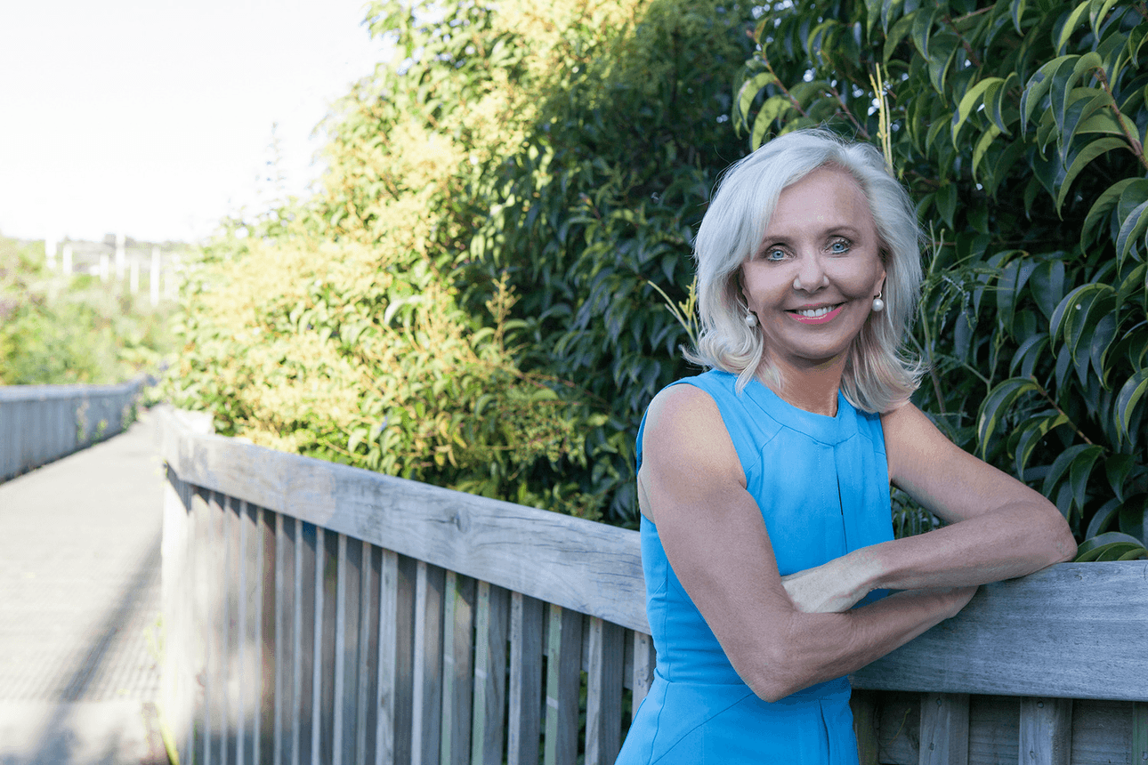 desley simpson in blue top on a wooden boardwalk with trees