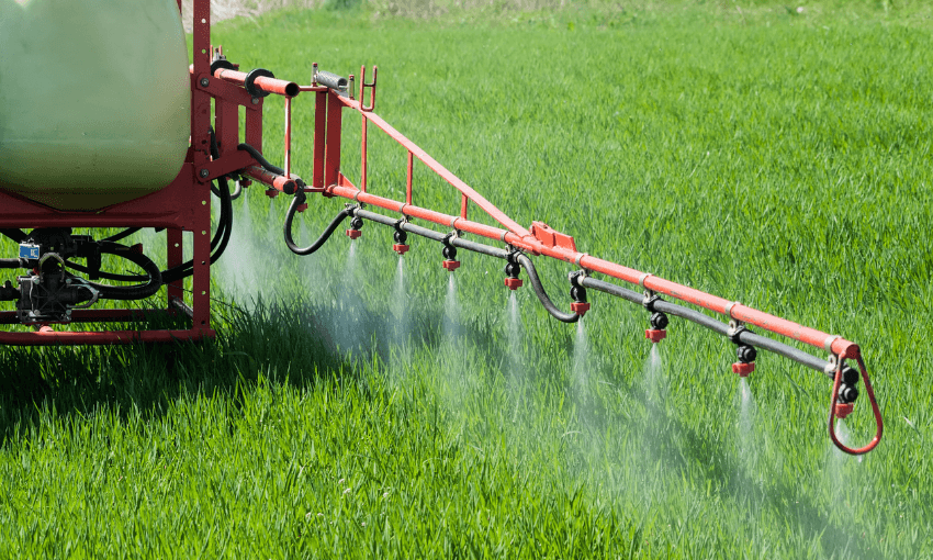 a red machine with lots of nozzles spraying a fine whit substance onto a verdant field