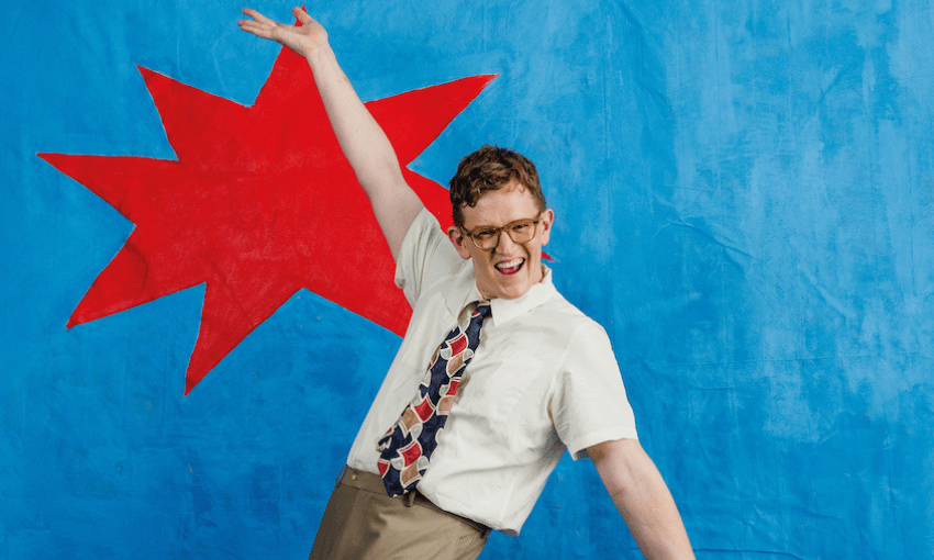 A man in a shirt and tie throws his arms up theatrically in front of a blue background with a red star on it