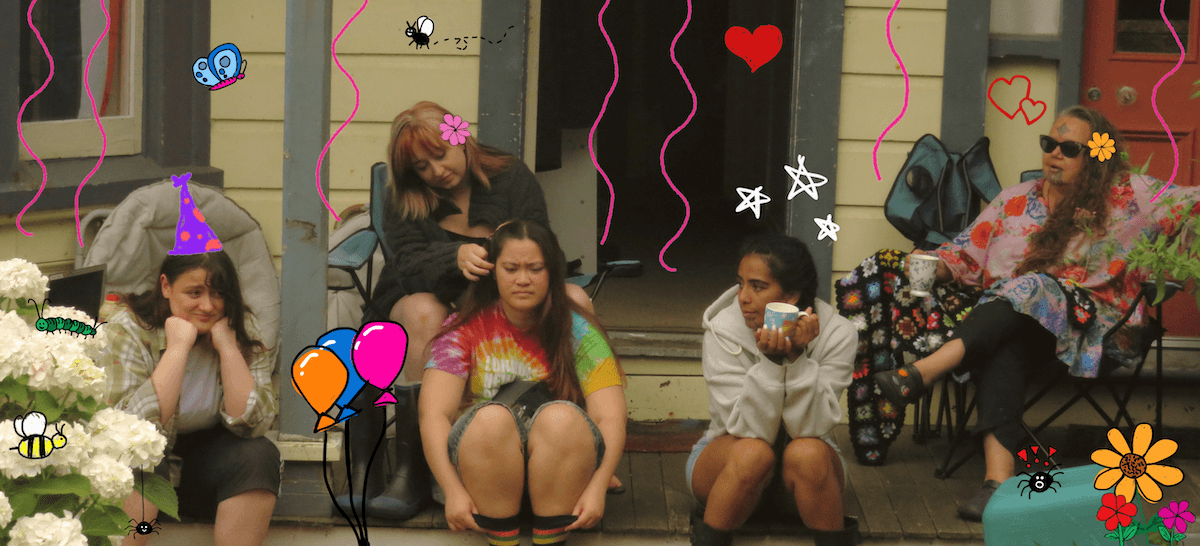 young adult girls on the front porch of a house, one drinking a cup of tea another braiding hair