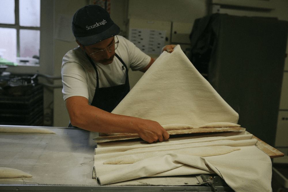 a baker in an artfully lit shot slides some uncooked baguette onto a tray 
