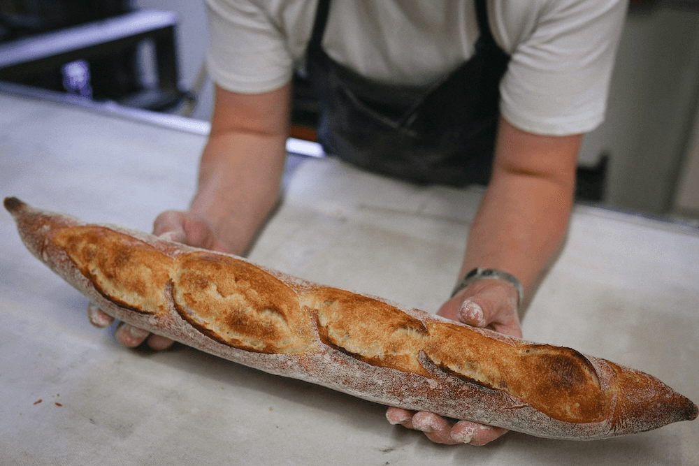 a burnished brown baguette balanced on a bakers hands