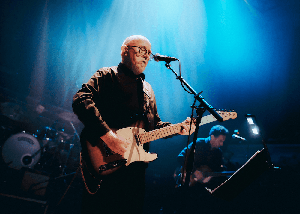 A photo of a man playing guitar and singing into a microphone on a stage.