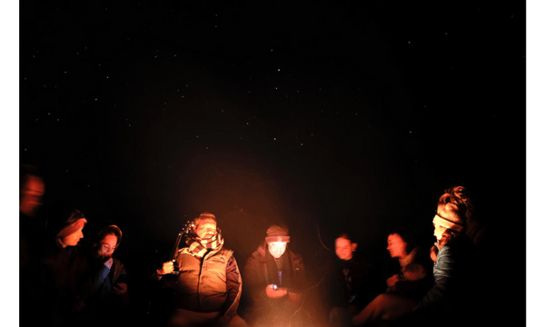 People huddled around a fire with the night sky showing stars above them.